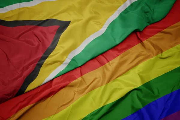 Machając kolorowe gej tęczowa flaga i Flaga Gujany. — Zdjęcie stockowe