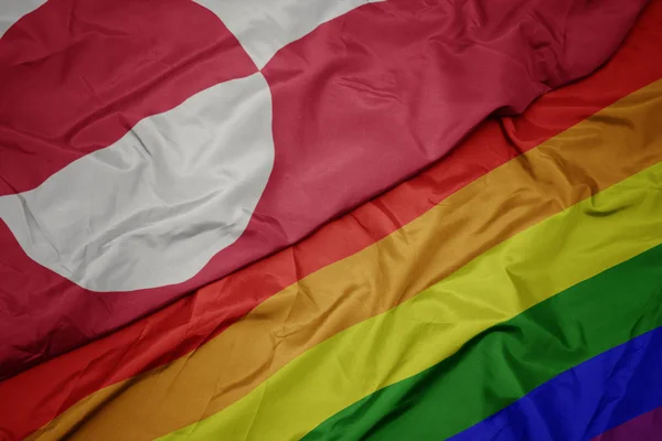 Waving colorful gay rainbow flag and national flag of greenland. — Stock Photo, Image