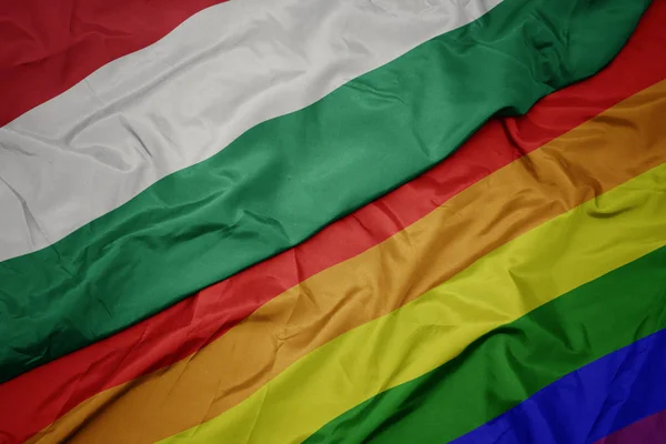 Falujące kolorowe gej tęczowa flaga i flaga Węgier. — Zdjęcie stockowe