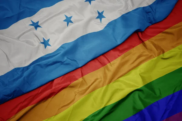 Zwaaiende kleurrijke Gay regenboog vlag en nationale vlag van Honduras. — Stockfoto