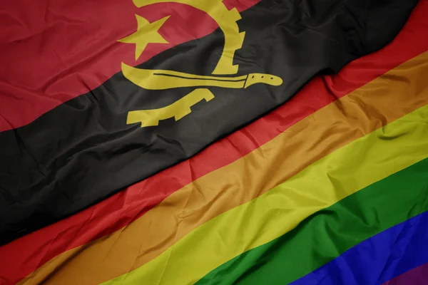 Vinka färgglada homosexuella regnbågens flagga och nationella flagga av Angola. — Stockfoto
