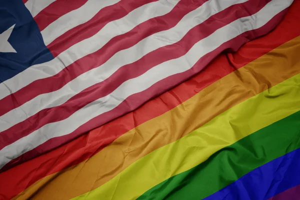 Waving colorful gay rainbow flag and national flag of liberia. — Stock Photo, Image