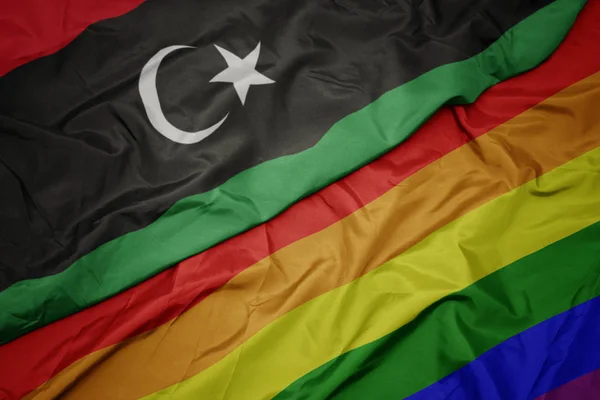 Waving colorful gay rainbow flag and national flag of libya. — Stock Photo, Image