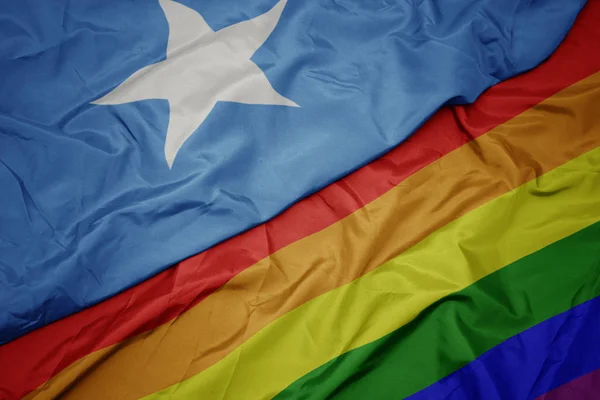Hullámzó színes homoszexuális Szivárvány zászló és a nemzeti zászló Szomália. — Stock Fotó