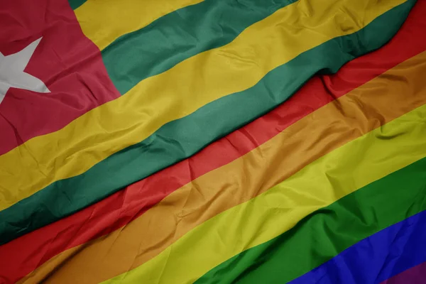 Waving colorful gay rainbow flag and national flag of togo. — Stock Photo, Image