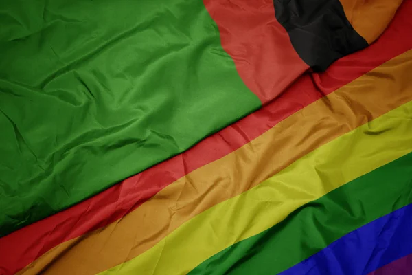 Ondeando colorida bandera arco iris gay y bandera nacional de zambia . — Foto de Stock