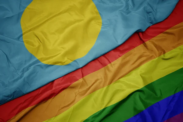 Waving colorful gay rainbow flag and national flag of Palau — Stock Photo, Image