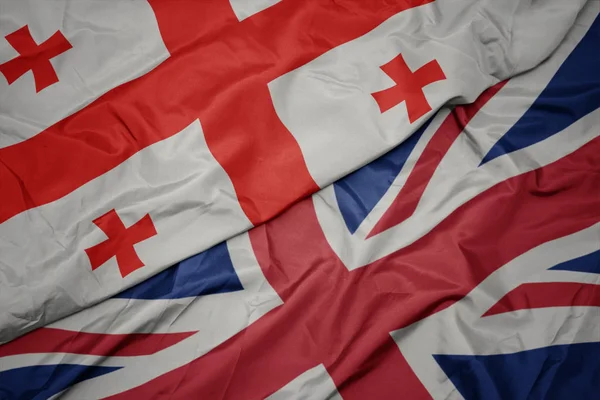 Zwaaiende kleurrijke vlag van Groot-Brittannië en de nationale vlag van Georgië. — Stockfoto