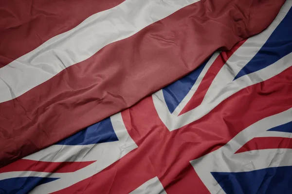 Mávající barevná vlajka Velké Británie a národní vlajky Lotyšska. — Stock fotografie