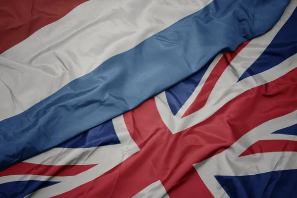 Zwaaiende kleurrijke vlag van Groot-Brittannië en de nationale vlag van Luxemburg. — Stockfoto