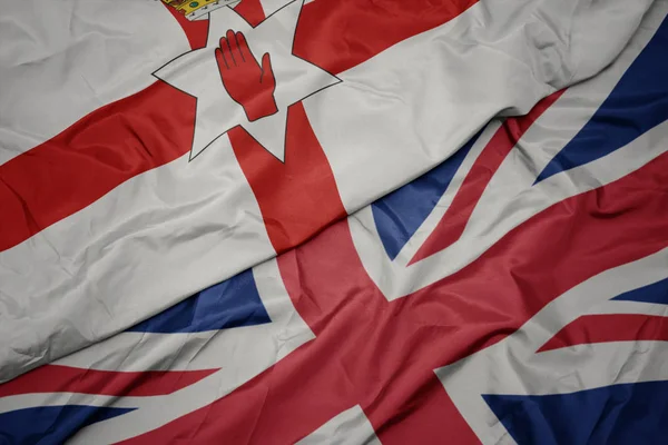 Zwaaiende kleurrijke vlag van Groot-Brittannië en de nationale vlag van Noord-Ierland. — Stockfoto