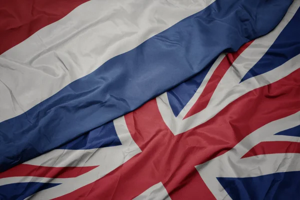 Zwaaiende kleurrijke vlag van Groot-Brittannië en de nationale vlag van Nederland. — Stockfoto
