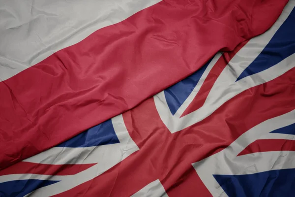 Zwaaiende kleurrijke vlag van Groot-Brittannië en de nationale vlag van Polen. — Stockfoto