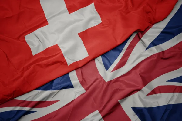 Zwaaiende kleurrijke vlag van Groot-Brittannië en de nationale vlag van Zwitserland. — Stockfoto