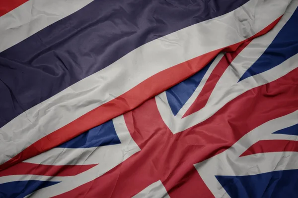 Zwaaiende kleurrijke vlag van Groot-Brittannië en de nationale vlag van Thailand. — Stockfoto
