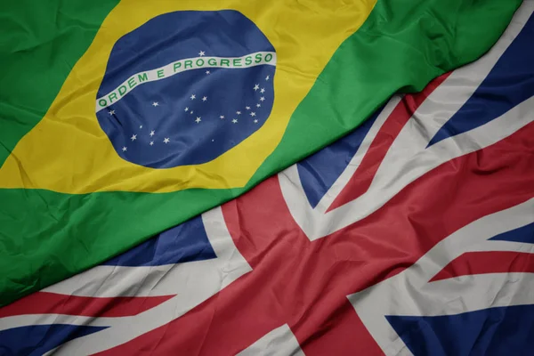 Ondeando colorida bandera de Gran Bretaña y bandera nacional de Brasil . — Foto de Stock