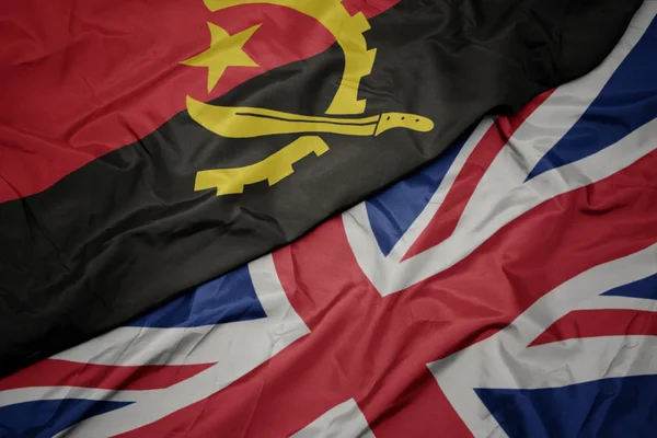 Acenando bandeira colorida de grande britânico e bandeira nacional de angola . — Fotografia de Stock