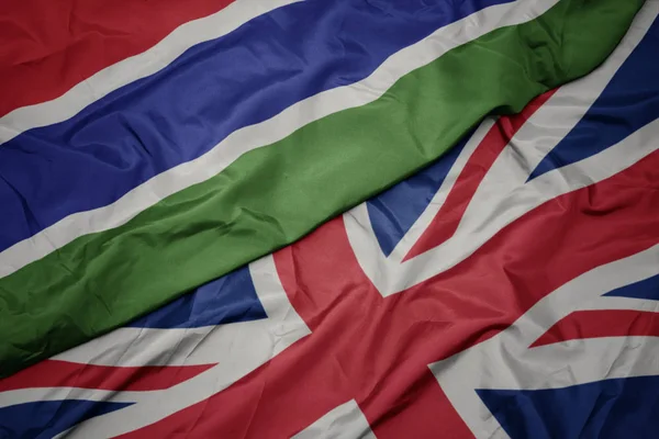 Zwaaiende kleurrijke vlag van Groot-Brittannië en de nationale vlag van Gambia. — Stockfoto