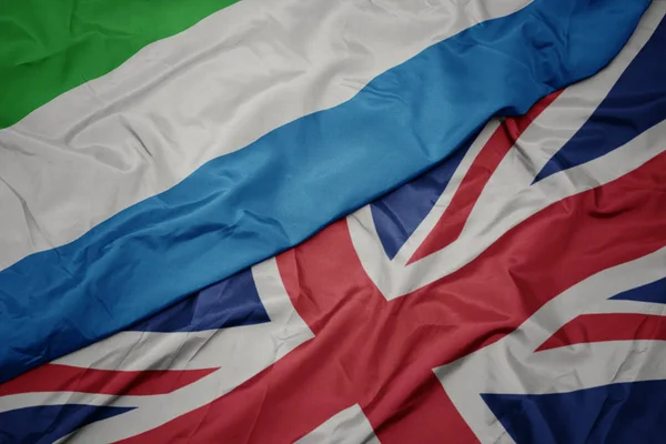 Zwaaiende kleurrijke vlag van Groot-Brittannië en de nationale vlag van Sierra Leone. — Stockfoto