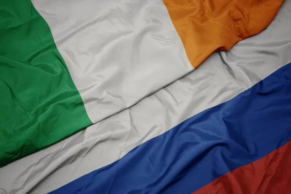 Acenando bandeira colorida da Rússia e bandeira nacional da Irlanda . — Fotografia de Stock