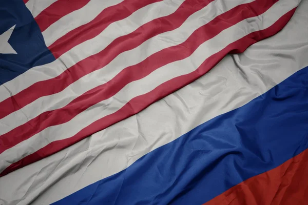 Falujące kolorowe flagi Rosji i Narodowej flagi Liberii. — Zdjęcie stockowe