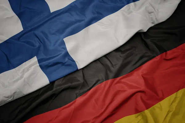 Acenando bandeira colorida da alemanha e bandeira nacional da Finlândia . — Fotografia de Stock