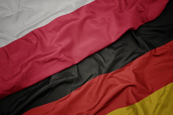 Mávající barvitá vlajka Německa a národní vlajky Polska. — Stock fotografie