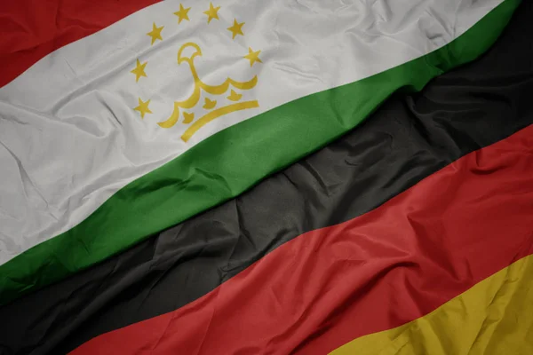 Waving colorful flag of germany and national flag of tajikistan. — Stock Photo, Image