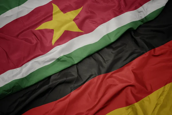 Ondeando colorida bandera de Alemania y bandera nacional de Surinam . — Foto de Stock