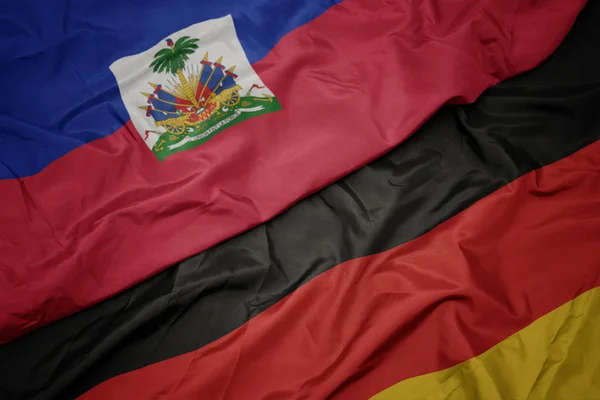 Zwaaiende kleurrijke vlag van Duitsland en de nationale vlag van Haïti. — Stockfoto