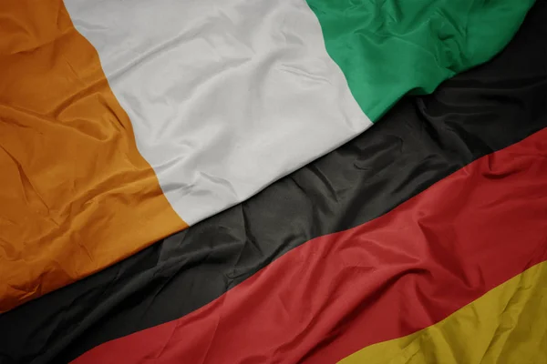 Acenando bandeira colorida da alemanha e bandeira nacional do cote divoire . — Fotografia de Stock