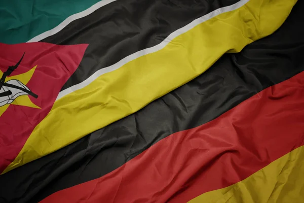 Acenando bandeira colorida da alemanha e bandeira nacional de moçambique . — Fotografia de Stock
