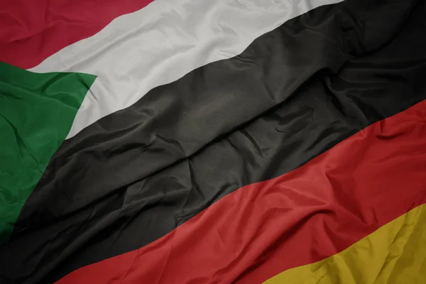waving colorful flag of germany and national flag of sudan.