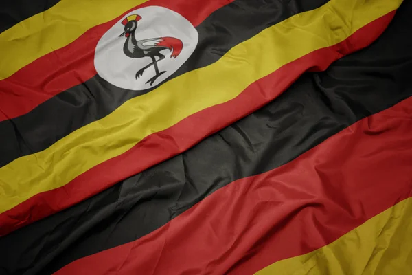 Sventolando bandiera colorata della Germania e bandiera nazionale di uganda . — Foto Stock