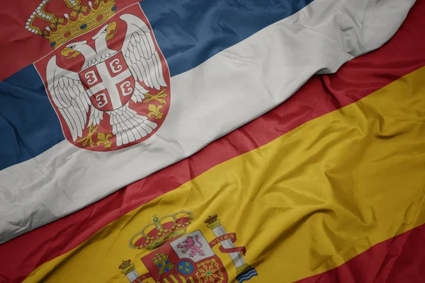 Vinka färgglada flagga av Spanien och nationella flaggan Serbien. — Stockfoto