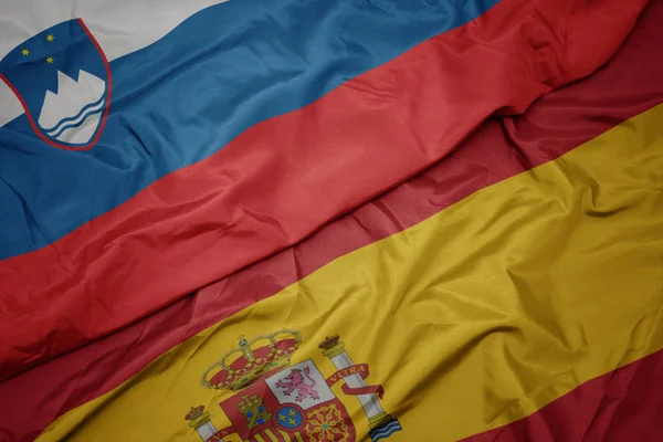 Ondeando colorida bandera de España y bandera nacional de slovenia . — Foto de Stock