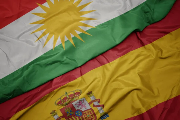 Κυματιστό πολύχρωμο σημαία της Ισπανίας και την εθνική σημαία του Κουρδιστάν. — Φωτογραφία Αρχείου