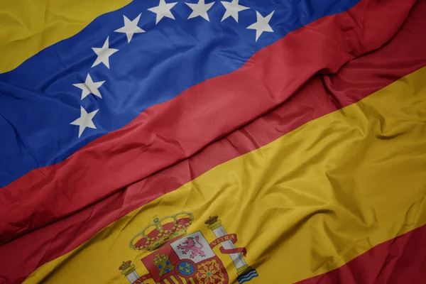 waving colorful flag of spain and national flag of venezuela.