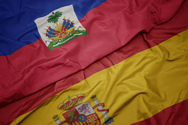 Zwaaiende kleurrijke vlag van Spanje en de nationale vlag van Haïti. — Stockfoto