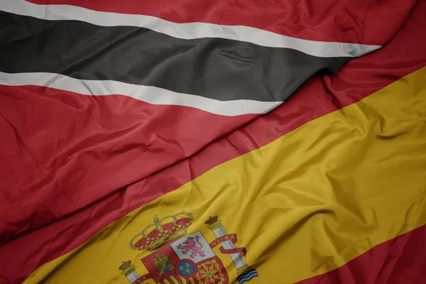 Falujące kolorowe flagi Hiszpanii i flagi narodowej Trynidadu i Tobago. — Zdjęcie stockowe