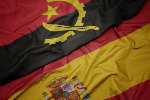 Waving colorful flag of spain and national flag of angola. — Stock Photo, Image