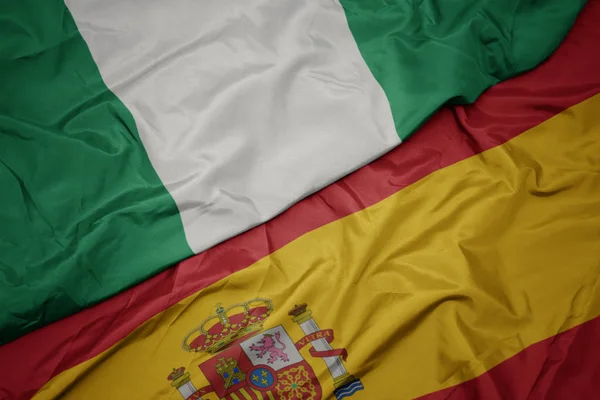 Vinka färgglada flagga av Spanien och nationella flaggan i Nigeria. — Stockfoto