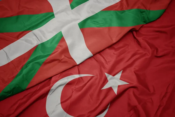 waving colorful flag of turkey and national flag of basque country.