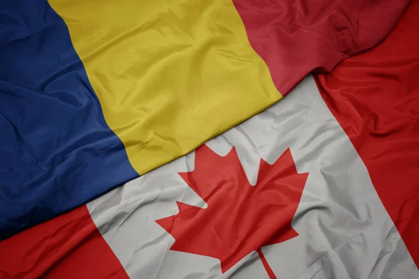 Zwaaiende kleurrijke vlag van Canada en de nationale vlag van Roemenië. — Stockfoto