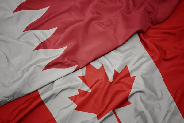 waving colorful flag of canada and national flag of bahrain.