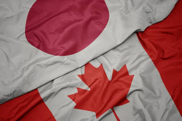 Zwaaiende kleurrijke vlag van Canada en de nationale vlag van Japan. — Stockfoto
