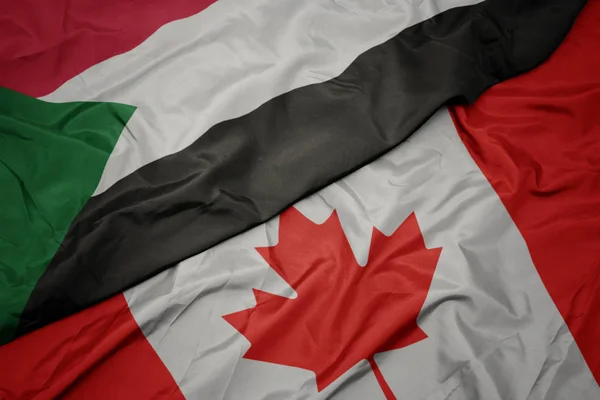 Acenando bandeira colorida do Canadá e bandeira nacional do sudan . — Fotografia de Stock