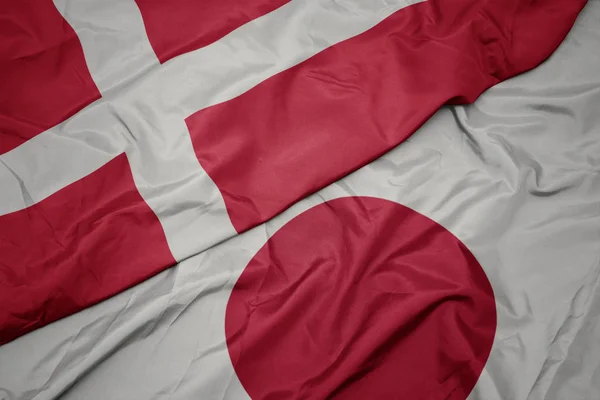 waving colorful flag of japan and national flag of denmark.