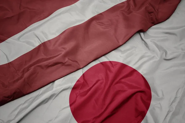 Zwaaiende kleurrijke vlag van Japan en de nationale vlag van Letland. — Stockfoto