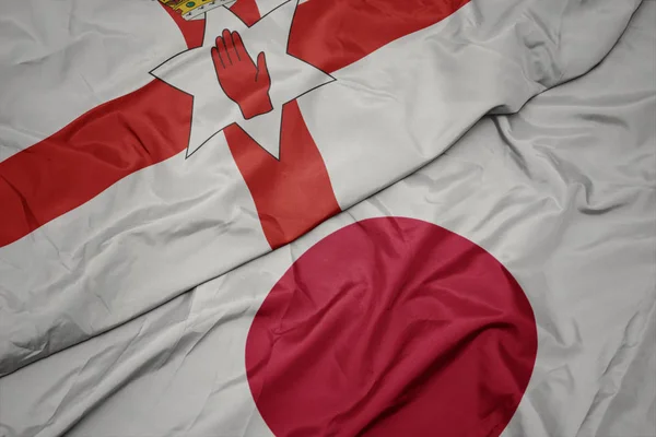 waving colorful flag of japan and national flag of northern ireland.